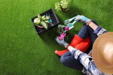 Woman potting flower on green grass, top view with space for text. Home gardening