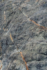 Weathered gray rock face with orange and white mineral veins as a nature background