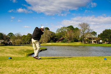 Golfer in action shot hitting with ball heading towards the pin hole over water