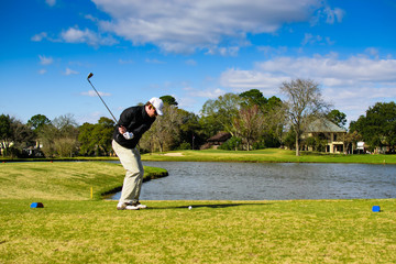 Golfer in action shot hitting with ball on tee in front of water