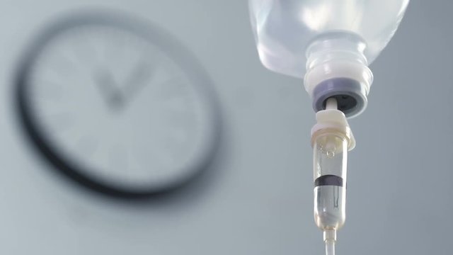 Intravenous drip chamber with office clock background