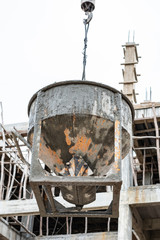 Crane lifting concrete mixer bucket container on construction site.