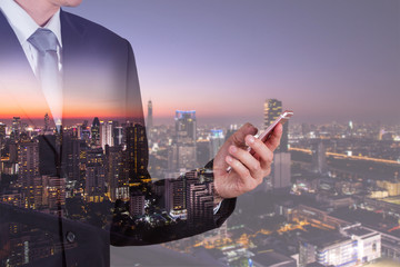 Double exposure of businessman use smartphone, communication networking telephone and cityscape urban in the night or twilight as business, technology, communication and telecom concept