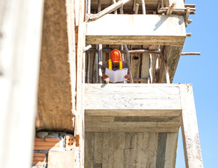 Asian architect or engineer holding looking project blueprint papers and wear helmet at construction site.