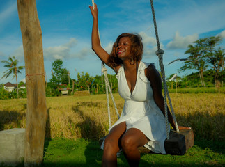 young happy and beautiful black African American woman in Summer dress playing outdoors on swing...