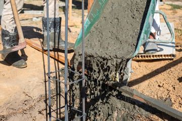 Naklejka premium Worker pouring cement mixture using a wheelbarrow in construction site.