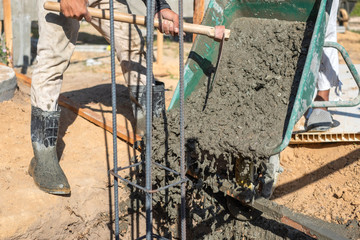 Worker pouring cement mixture using a wheelbarrow in construction site.