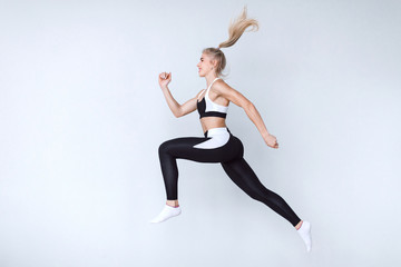 Fototapeta na wymiar Full length fitness woman jumping agains gray background.