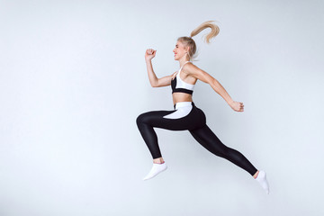 Fototapeta na wymiar Fit young woman jumping against grey background. Female model in sports wear jumping.