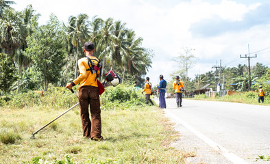 Male worker with grass cutter / brush cutter cut grass at road side. Gardening concept.