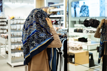 Thai muslim woman trying hijab in front of mirror at shopping mall. Selective focus. Shopping and fashio concept.
