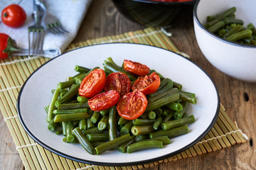Green beans with baked cherry tomatoes on a wooden background