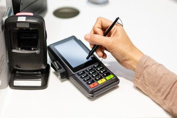 Close-up of consumer's hand signing on a touch screen of credit card sale transaction receipt machine.