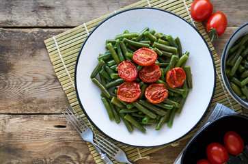 Green beans with baked cherry tomatoes on a wooden background