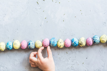 Children's hand holding colorful easter eggs which lying on gray concrete background. Flat lay. Top view. Holiday concept.