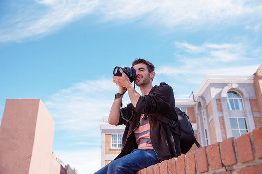 Young man sitting on a wall shooting photos of the town