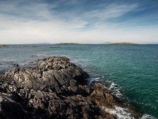 Sunny day on West coast of Ireland, blue sky and water, grungy rock coast.