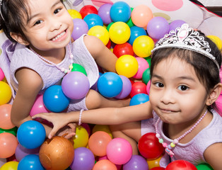 Fototapeta na wymiar Female asian identical twins sitting on chair with white background. Wearing purple dress and accessories. Playing colorful plastic toy balls