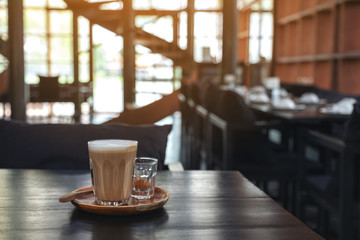 Closeup image of a glass of hot coffee on wooden table in cafe