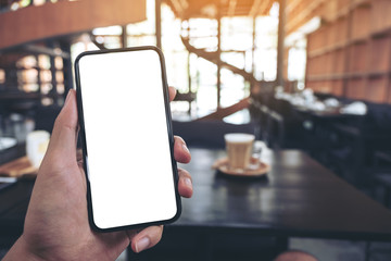 Mockup image of a man's hand holding black mobile phone with blank screen with a glass of coffee on wooden table in cafe