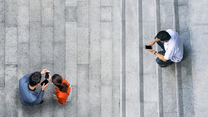 the top aerial view of the man in white shirt uses mobile phone and sits with businessman and woman people meeting and using smartphone for presentation at outdoor pedestrian city.