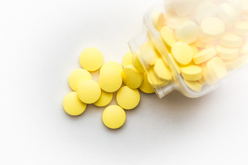 Yellow pills scattered from a glass jar on a white background.