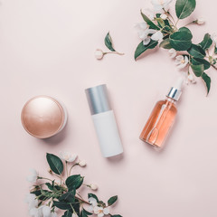 Pink natural cosmetics: oil, serum, cream, mask on background with flowers. Flat lay, minimalism.