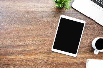 Big tablet with blank screen is on top of wood office desk table with supplies. Top view with copy...