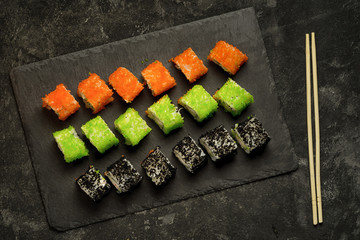 Top view set of assorted japanese sushi food on a black stone plate and sushi sticks. Rolls with tuna, salmon, shrimp, crab and avocado. Sushi menu.