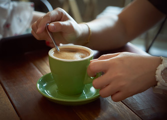 Unknown female hand stirring a cup of coffee in the morning on wooden table