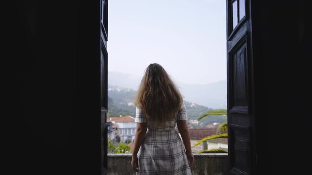Following from back young lady opening doors in dark room and going on balcony of traditional country house. Valley of Douro river in winemaking region in Portugal