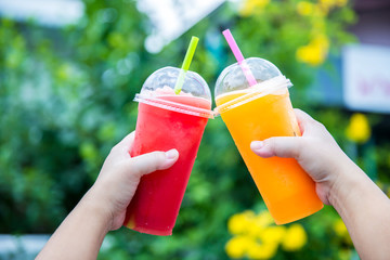 Fruit Smoothie. Hand holding plastic cup of colourful fruit smoothie at cute cafe. Hand holding plastic cup with delicious smoothie on nature background. hand holding glass with delicious smoothie.