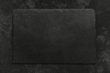 Black on black. Empty black granite stone rectangle board on black textured cement background, top...