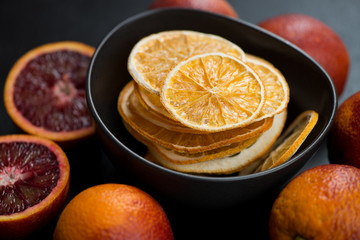 Bowl of orange fruit chips with fresh blood oranges around, horizontal shot