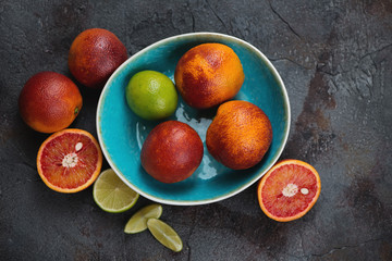 Sicilian blood oranges and limes in a turquoise bowl, above view on a grey asphalt background, horizontal shot
