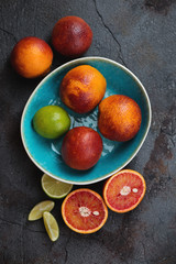 Turquoise bowl with blood oranges and limes, flatlay on a grey asphalt background, vertical shot