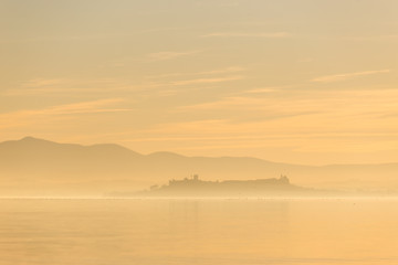 Beautiful view of Trasimeno lake at sunset with birds on water and Castiglione del Lago town