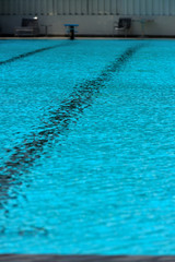 A swimming pool with a sunny reflection and beautiful wavy water surface in turquoise blue color with grab bars ladder on the sides and black line lanes underwater.