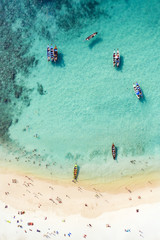 View from above, aerial view of a beautiful tropical beach with white sand and turquoise clear water, long tail boats and people sunbathing, Freedom beach, Phuket, Thailand.