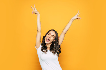 Are you ready?! A photo of vigorous young girl near the spicy-orange background showing “peace”...