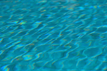 A swimming pool with a sunny reflection and beautiful wavy water surface in turquoise blue color with grab bars ladder on the sides and black line lanes underwater.