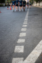 White dot lines of a street with a group of runners from the city mini marathon in a background. 