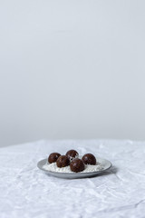 Homemade vegan chocolate candies with  grated coconut, nuts, cocoa on a white background with copy space