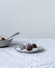 Homemade vegan chocolate candies with  grated coconut, nuts, cocoa on a white background with copy space