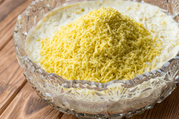 The process of cooking fish layered salad Mimosa. Laying grated egg yolk.