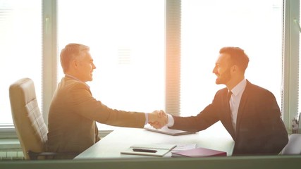 The two businessmen handshaking over the desk. slow motion