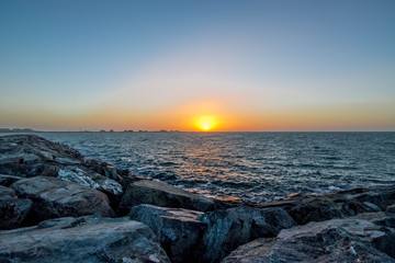 Beautiful Sun View in Beach from rock stone island shore with orange sky and yellow light reflection on sea water waves