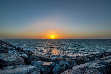 Obraz premium Beautiful Sun View in Beach from rock stone island shore with orange sky and yellow light reflection on sea water waves
