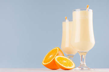 Sweet cheerful oranges milkshakes in two glass decorated slices fruit, striped straws on light pastel blue background.