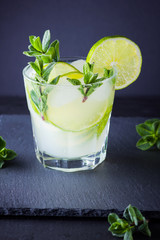 Cocktail mojito and mint on black background. Refreshing cocktail with lime and fresh mint on slate board. Summer drink with citrus and ice